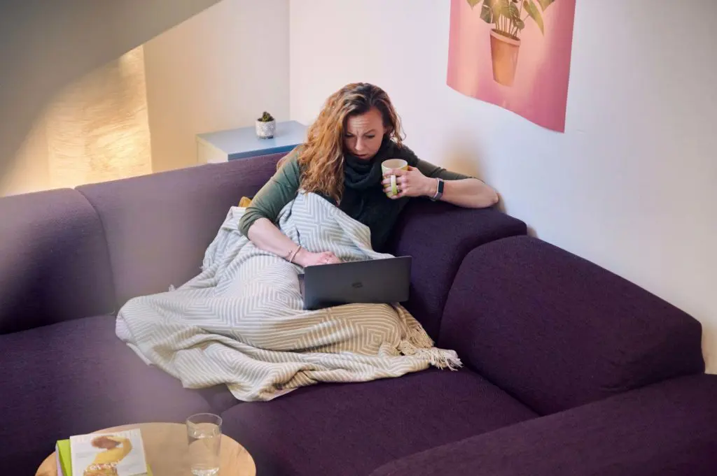 Kranke Frau sitzt auf Couch und bucht Termin in der Smartpraxis
