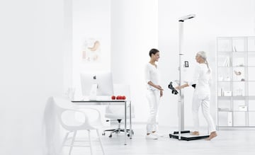 Ein Arzt und ein Patient stehen neben einem Bioimpedanzgerät für eine Messung der Körperzusammensetzung.